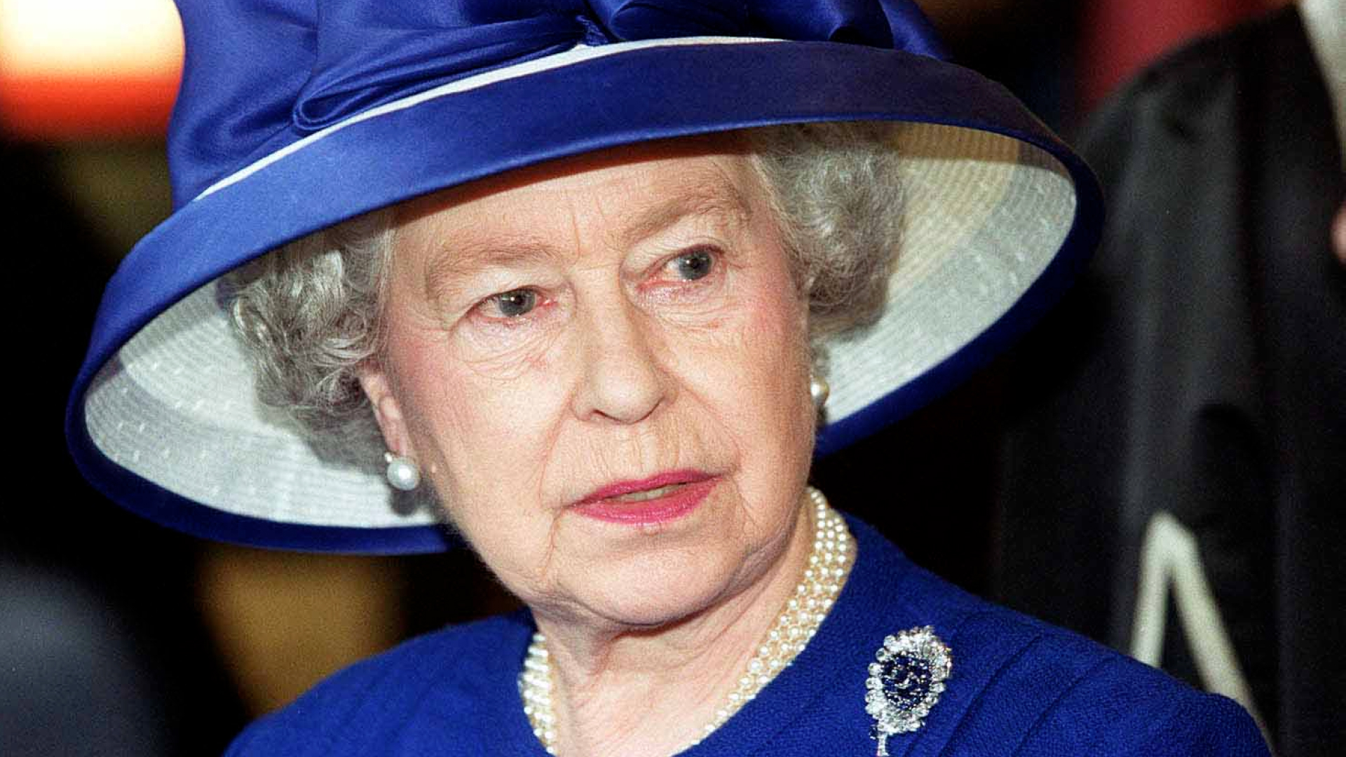 Britain's Queen Elizabeth II during a visit to Fitzalen High School wearing a royal blue suit with a matching wide-brim hat, a pearl necklace, and a sapphire and diamond brooch