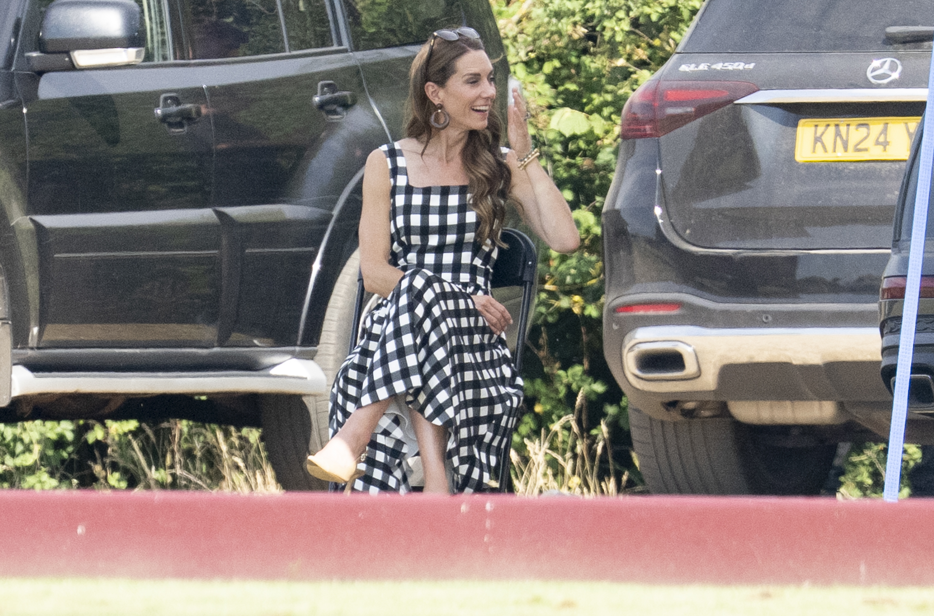 Princess Kate sitting in front of cars in a gingham dress
