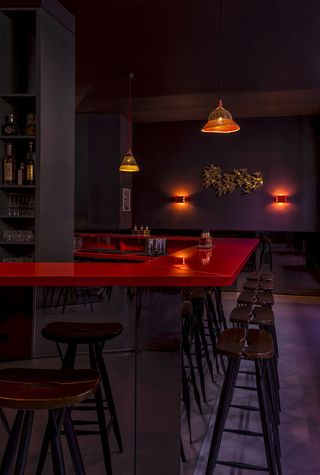 Maxie bar with red top and wooden bar stools, mauve walls with brass wall lamps