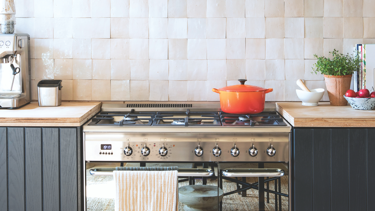 Silver oven with orange dutch oven on top. It has wood sideboards with black cupboards.