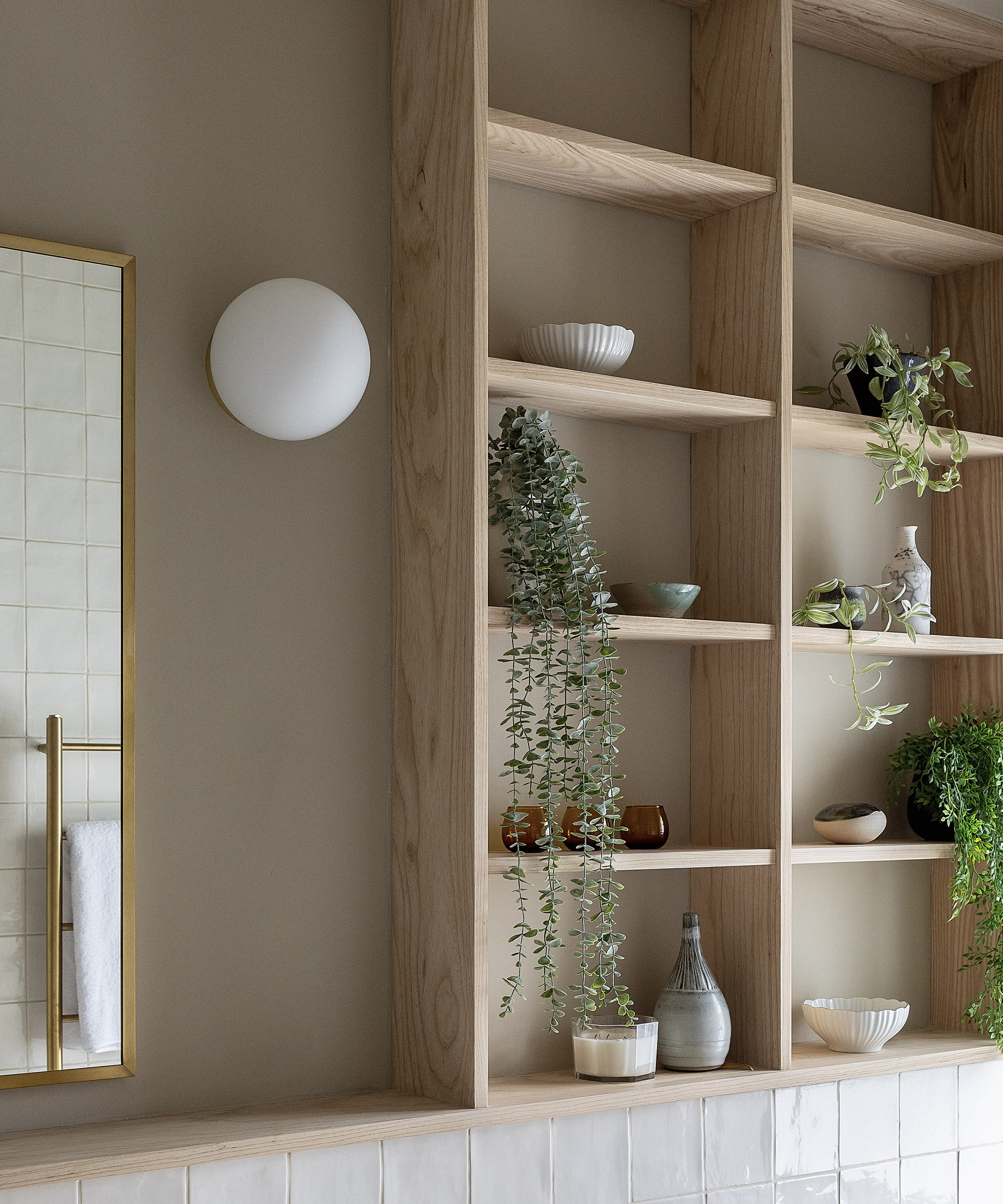Built in light wood shelves in a bathroom with houseplants and ornamental trinkets
