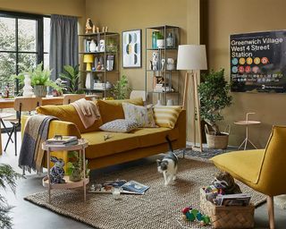 An open-plan living room with mustard yellow sofa decor, wooden floor lamp with white lampshade, jute woven rug, wooden side table and pair of modular shelves