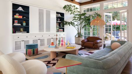 LALA Reimagined designed living room with white walls, green sofa, white armchair, round wooden coffee table, brown leather armchair and colorful rug with built-in storage