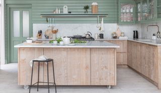 a wood kitchen with long kitchen island, marble backsplash and countertop and sage green walls