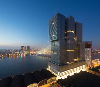 A dusk photo overlooking the Rotterdam Wilhemina Pier, featuring a high rise building.