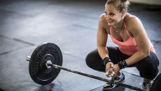 Woman squatting next to barbell and smiling