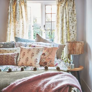 A bedroom with a bed with many throw floral throw pillows and floral curtains