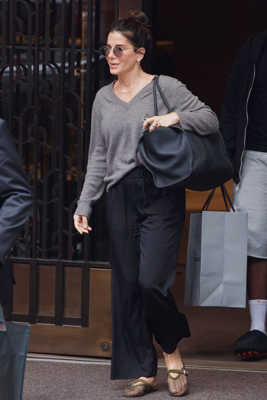 Sandra Bullock wearing a gray V-neck sweater, black pants, and mesh flats