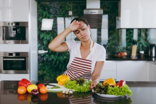 A person in the kitchen preparing a healthy meal looking tired.