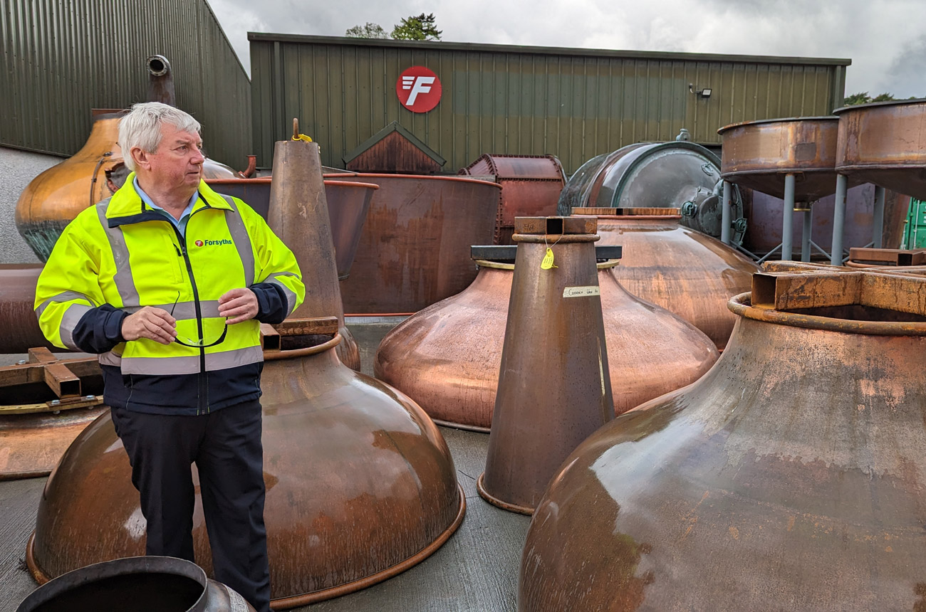 A man standing by whisky stills in a yard