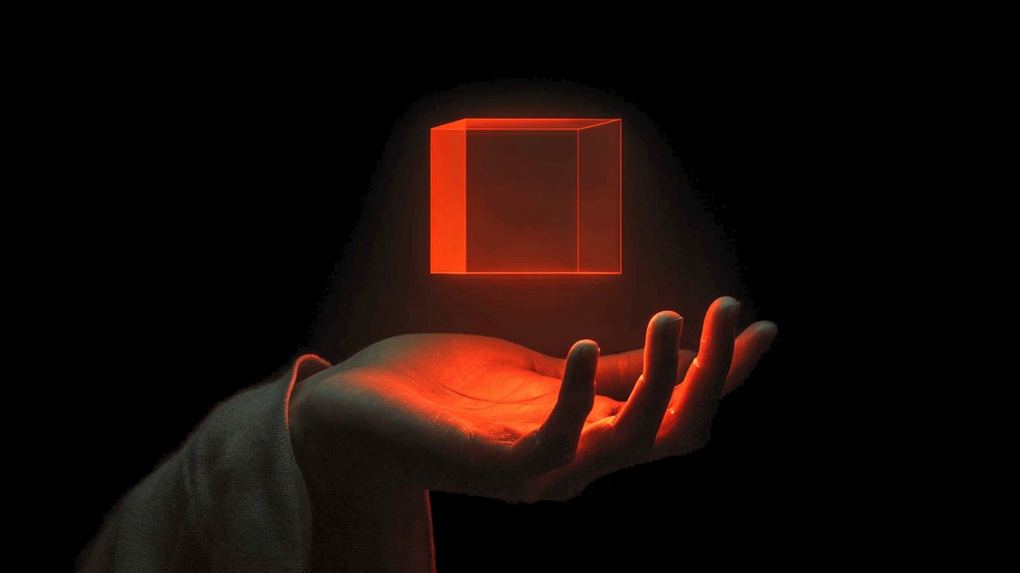 A hand over a dark background, with a see-through cube hovering over it