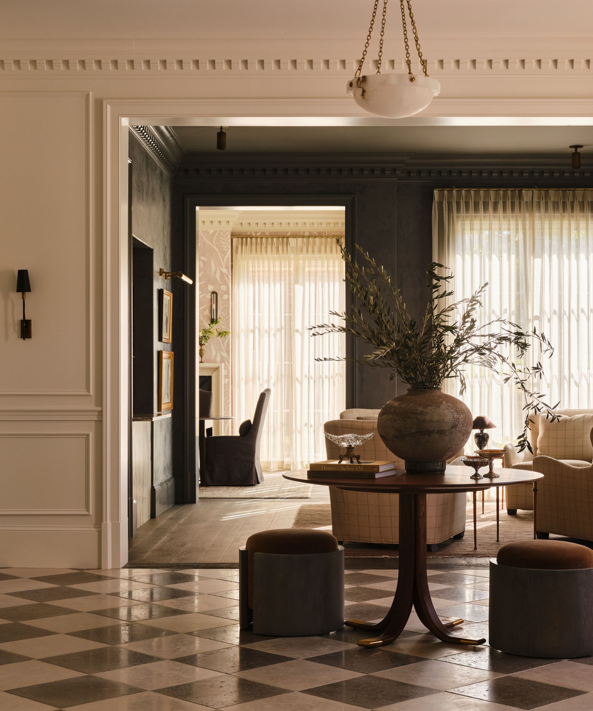 a neutral warm foyer with marble checkerboard flooring, detailing molding and paneling, a wooden circle table and small stools