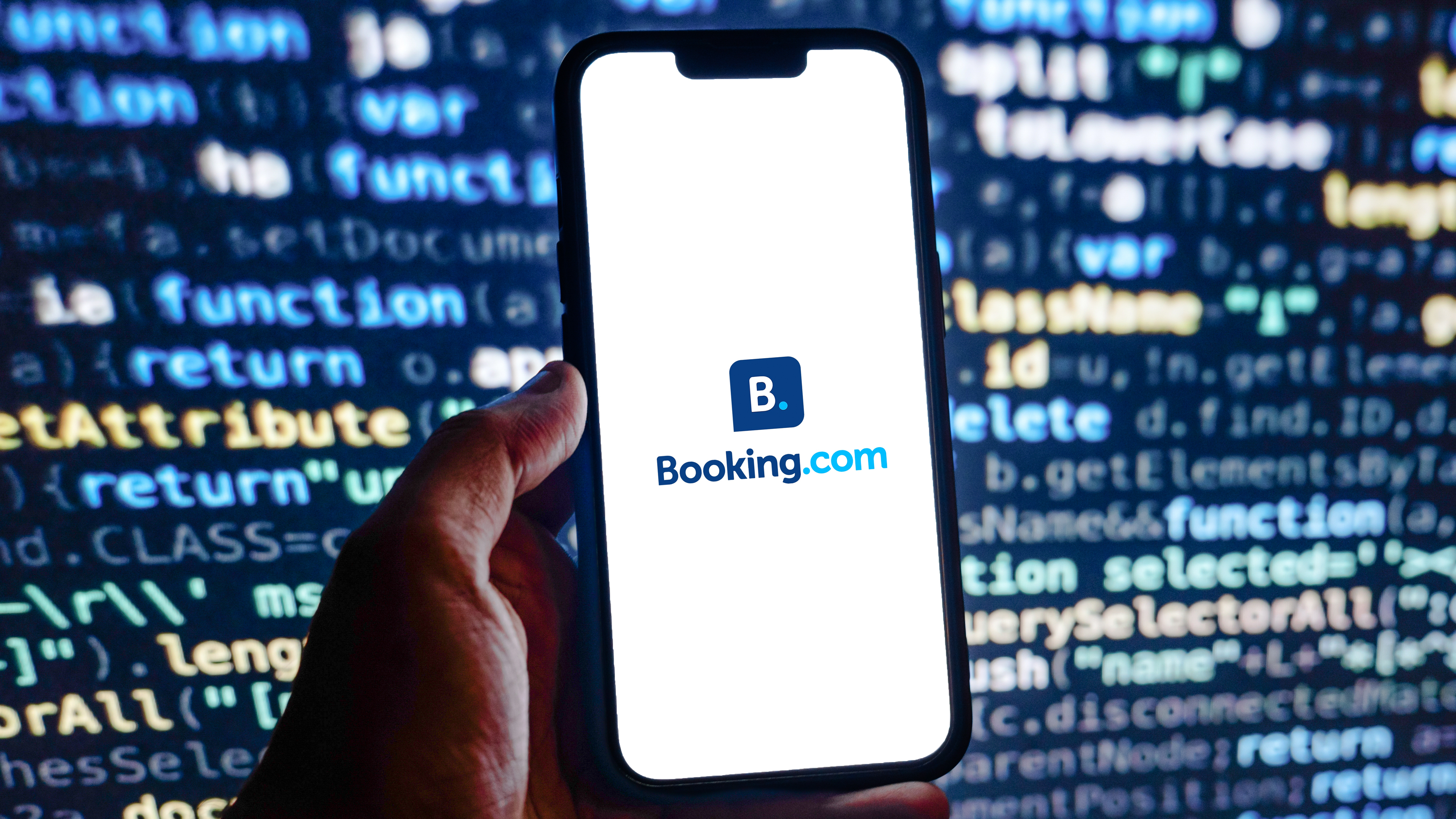 Booking.com logo on a smartphone in front of a screen of computer code