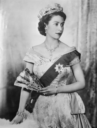 A black and white photo of Queen Elizabeth wearing a gown, sash and tiara looking to the right