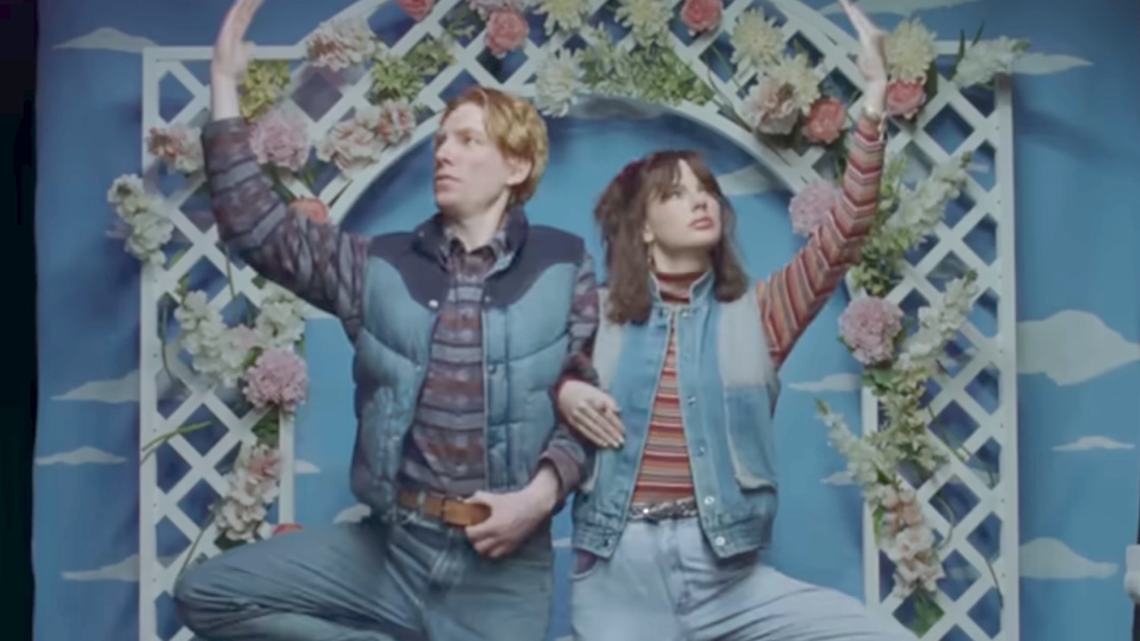 Domhnall Gleeson and Taylor Swift posing in front of a cloud backdrop in the Opalite music video