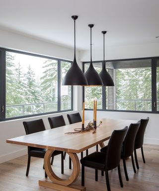 Modern, wooden dining table with black seating and semi-matching trio of ceiling lights