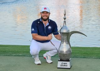 Tyrrell Hatton crouches down next to the 2025 Dubai Desert Classic trophy