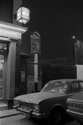 Black and white image of a car parked outside a pub at night