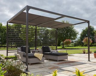 Modern pergola with retractable ceiling panels, over a patio area with plans and two brown sun loungers on it