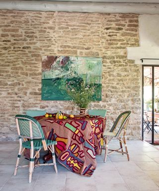 dining area with exposed stone wall, green painting, multi colored, patterned tablecloth and green bistro dining chairs