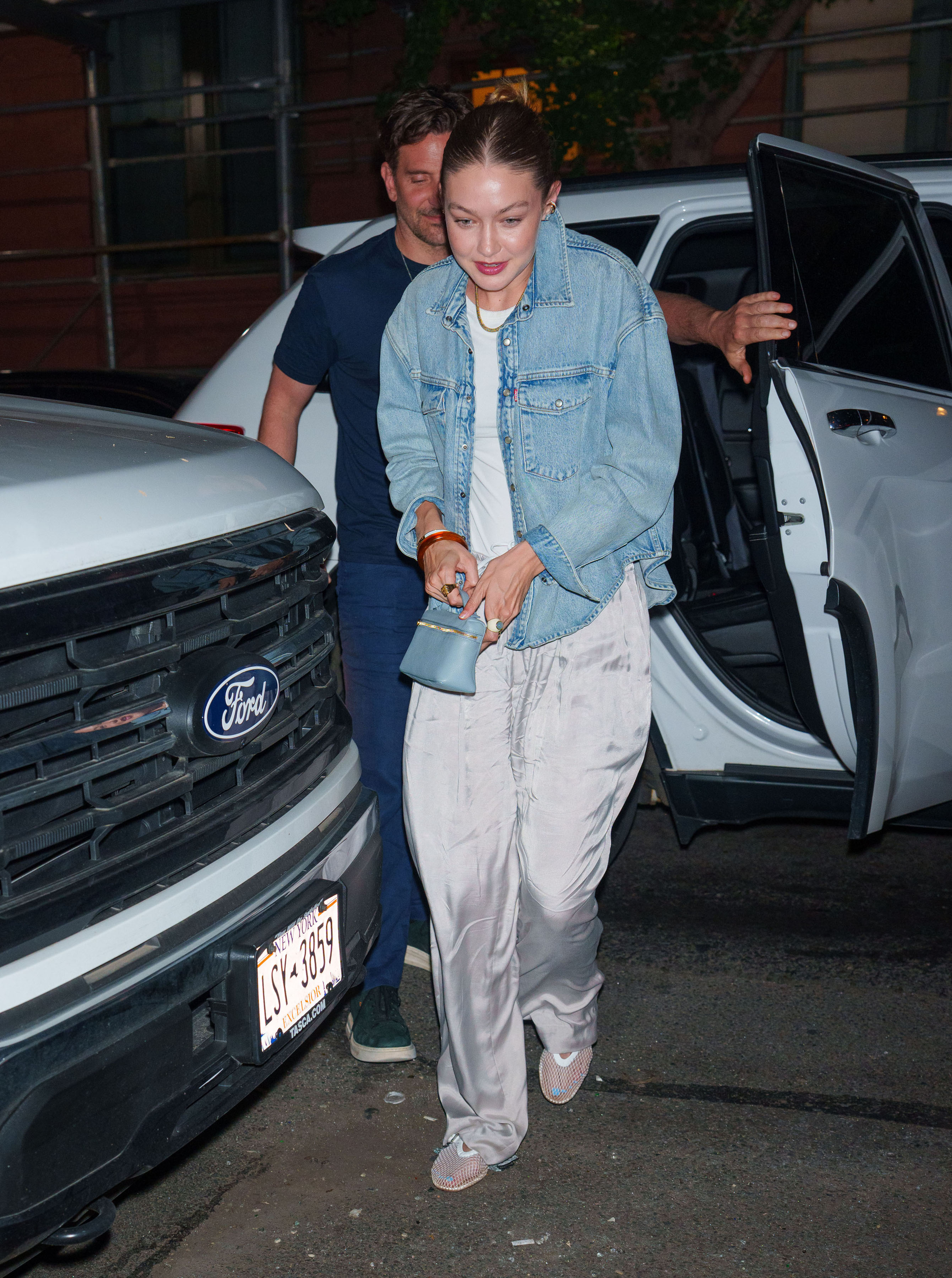 Gigi Hadid wearing a denim jacket, metallic track pants, and mesh flats