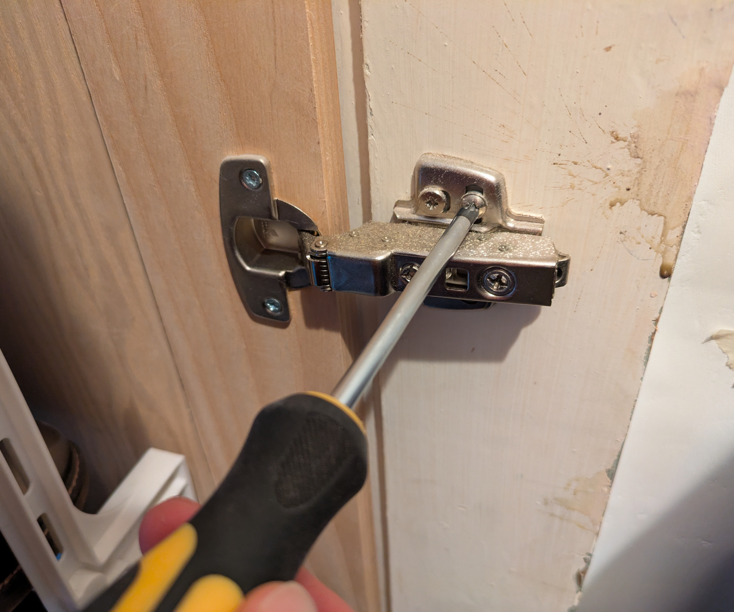 A screwdriver adjusting the screws in a door hinge