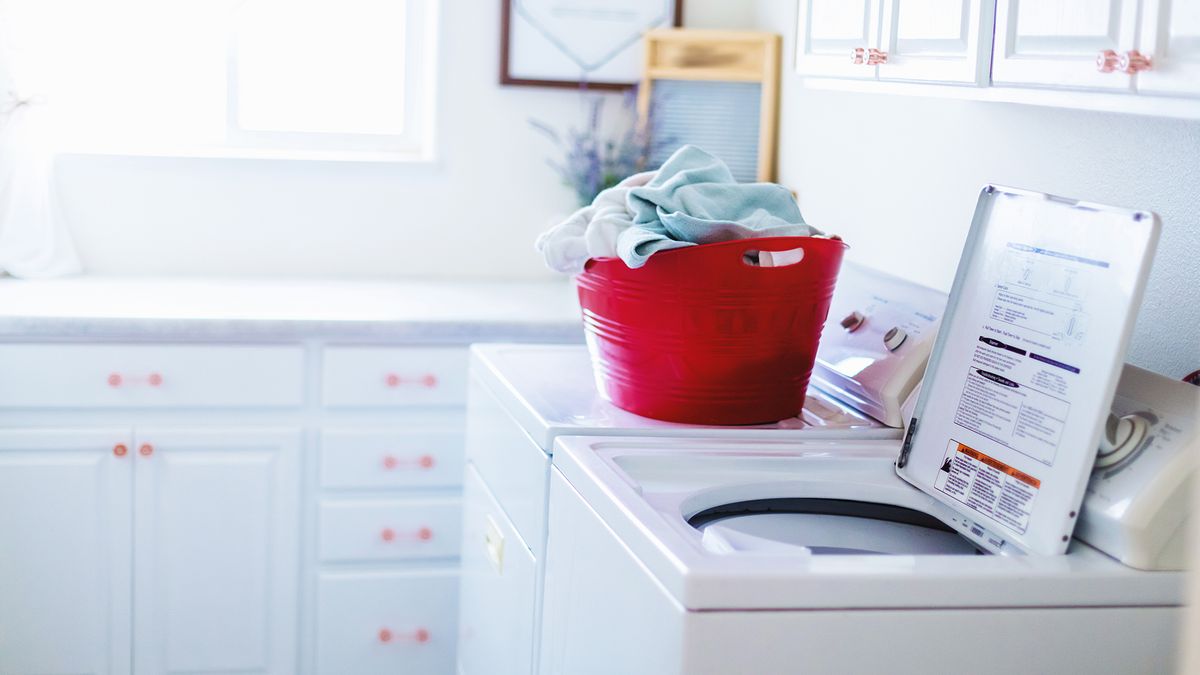 White top load washer in a utility room with red basket on top. 