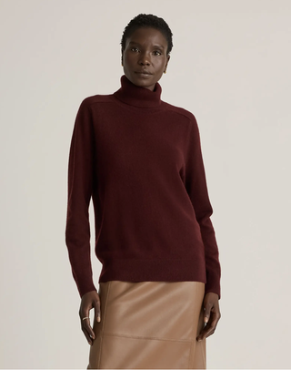 A model wearing a burgundy turtleneck sweater with a tan leather skirt