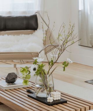 Japandi living room decorated with warm neutrals. The coffee table is made from natural wood tones, topped with a lively green houseplant, while the sofa in the backfround is whaite and dressed with neutral textiles