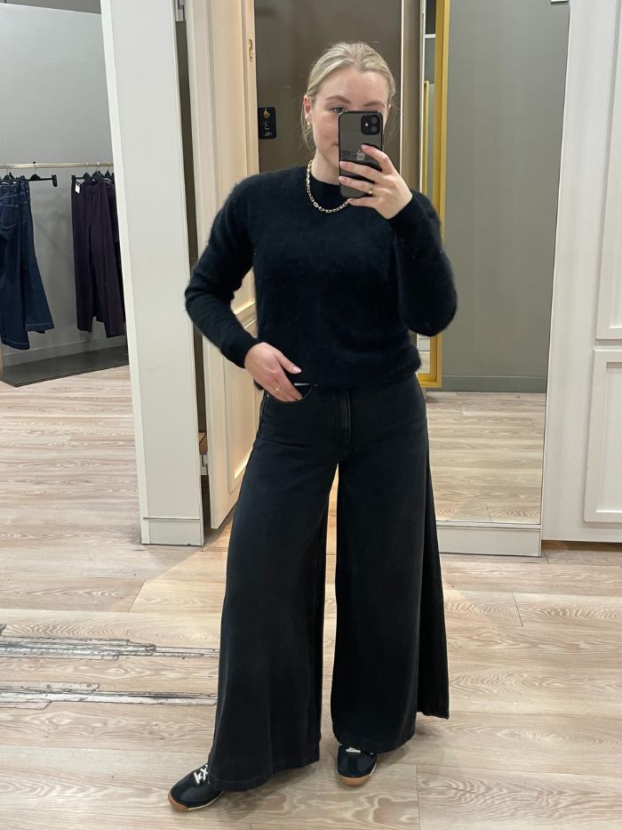 Woman wears wide palazzo jeans, black cashmere jumper and black trainers