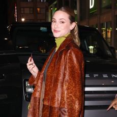 Lili Reinhart wearing a leather coat, jeans, and green accessories