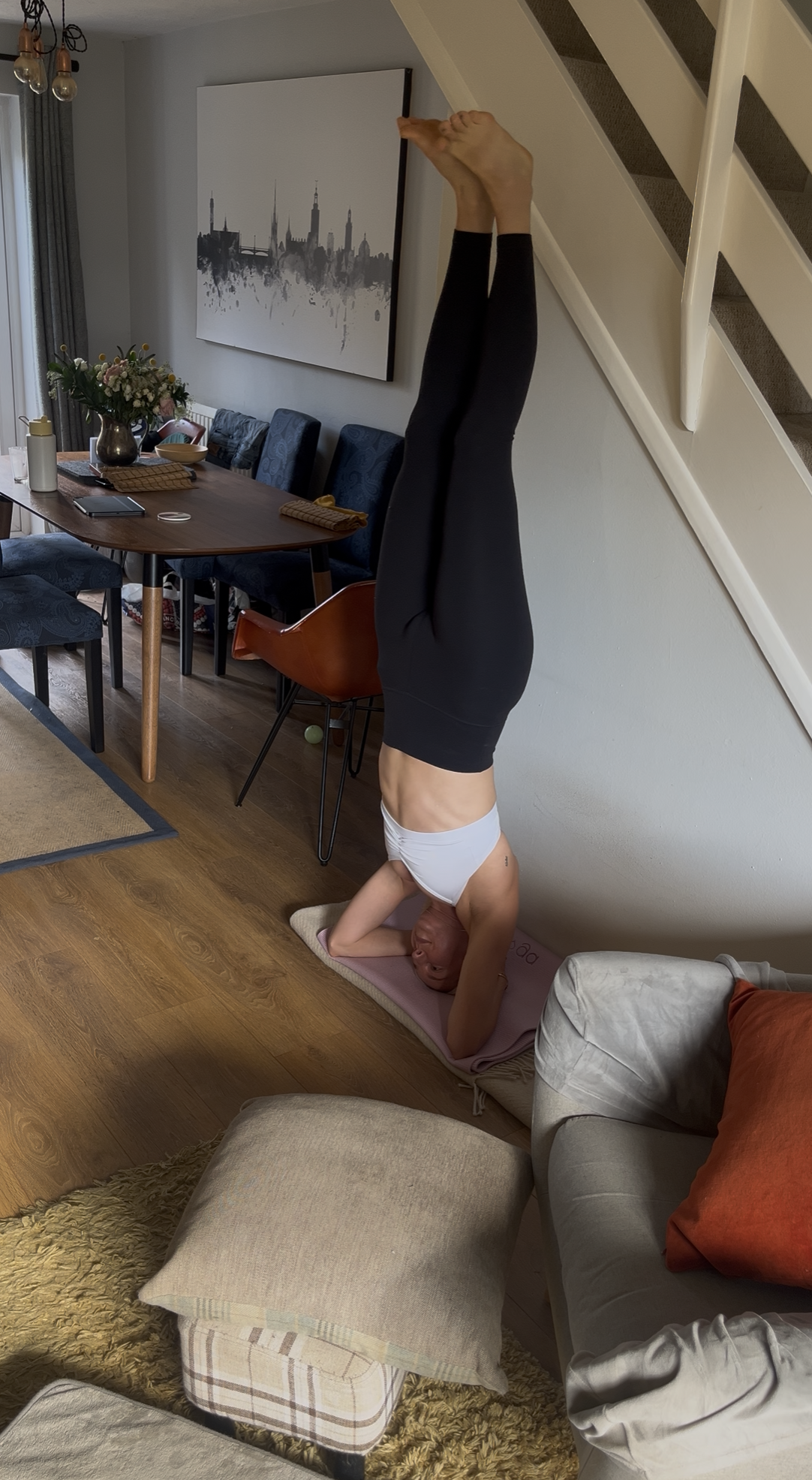 A woman practices a headstand at home with her hands behind her head