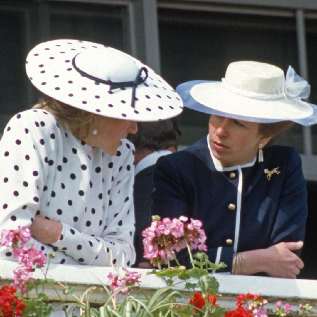 Princess Diana wearing a white polka dot dress and matching hat leaning forward to talk to Princess Anne wearing a blue jacket and white wide brimmed hat