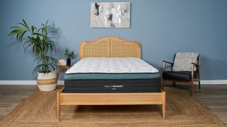The image shows the Helix Sunset Luxe Mattress on a wooden frame against a blue bedroom wall