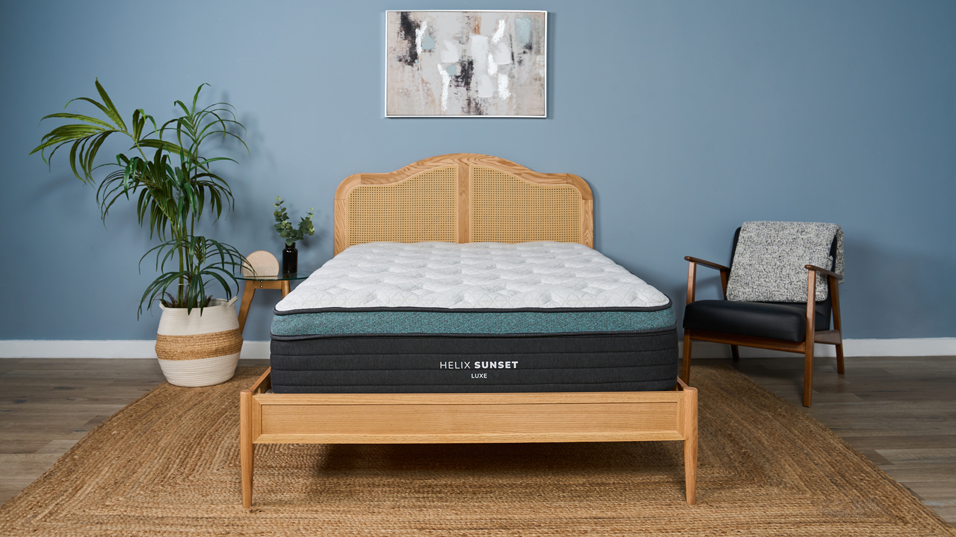 The image shows the Helix Sunset Luxe Mattress on a wooden frame against a blue bedroom wall