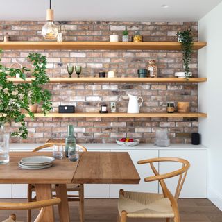 dining area with wishbone chairs, exposed brick wall with inset open shelving