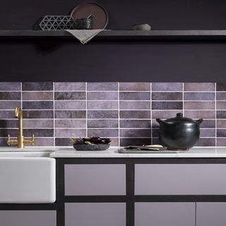 kitchen with purple walls, lavender and lilac tiles with a grey shelf and black pot