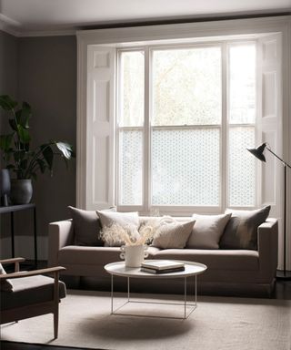 A serene living room featuring a large sash window adorned with subtle Japanese Asanoha patterned window film, allowing natural light to filter through while maintaining privacy.