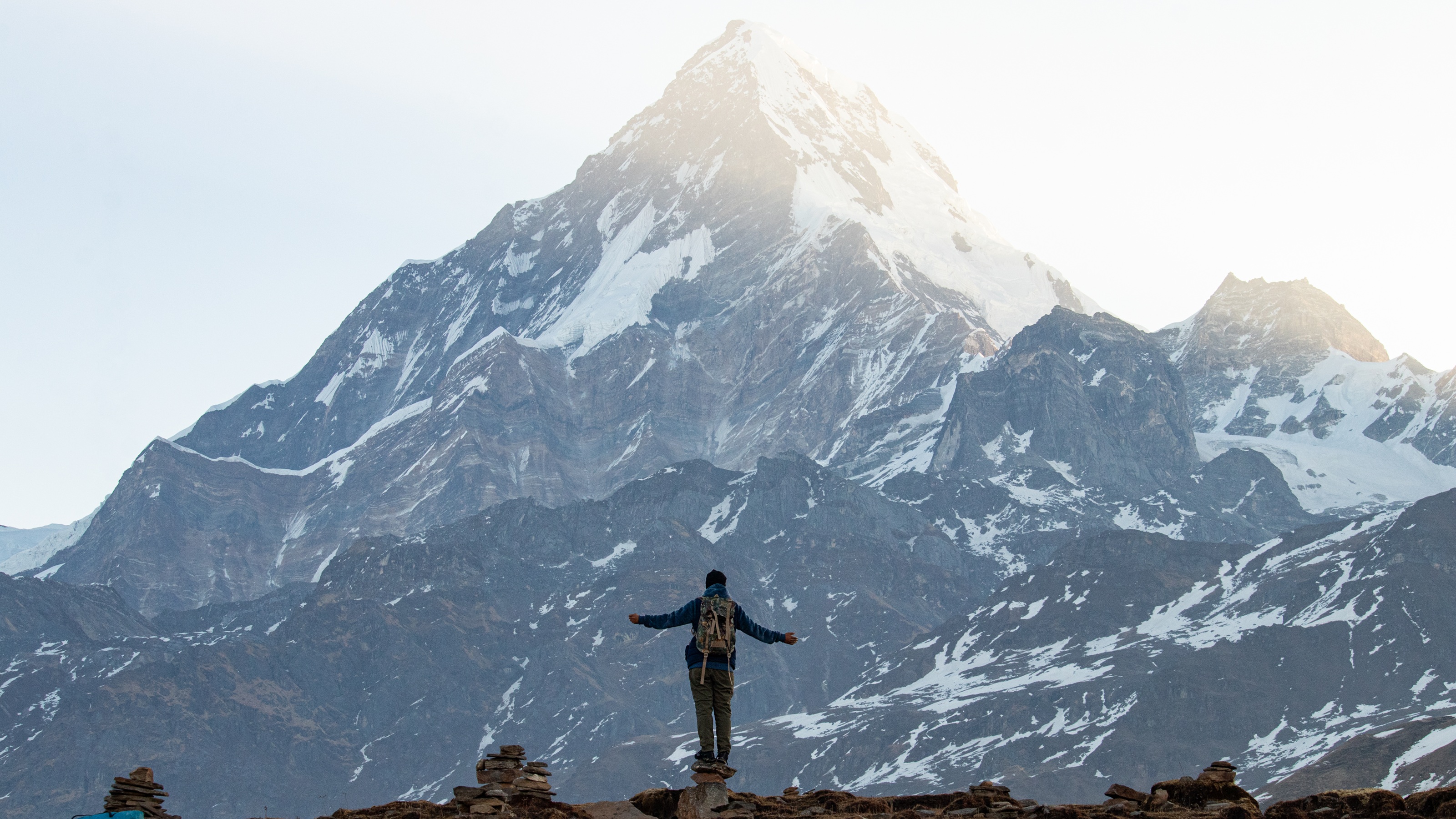 A hiker faces Mount Everest with arms spread.