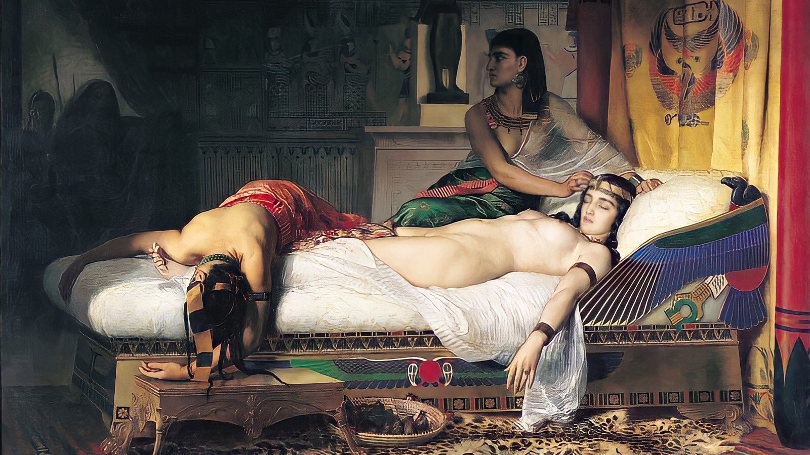 This is a painting called The Death of Cleopatra (1874) by Jean-André Rixens. Cleopatra is lying dead on a bed. She has long black hair and is wearing a gold headpiece. There is another dead body at the end of the bed and a person sitting over her, brushing Cleopatra's hair out of her face.