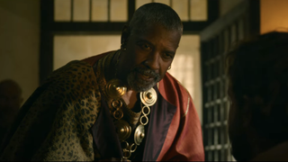 Denzel Washington crouched over and looking very intense, dressed in robes, for Gladiator 2 trailer.