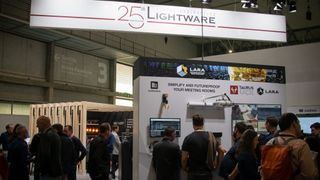 A group around Lightware's booth with a sign celebrating its 25th anniversary.
