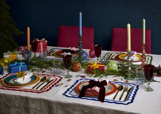 Christmas table setting with foliage garland, baubles, table placemats, candles, table presents, tree in corner