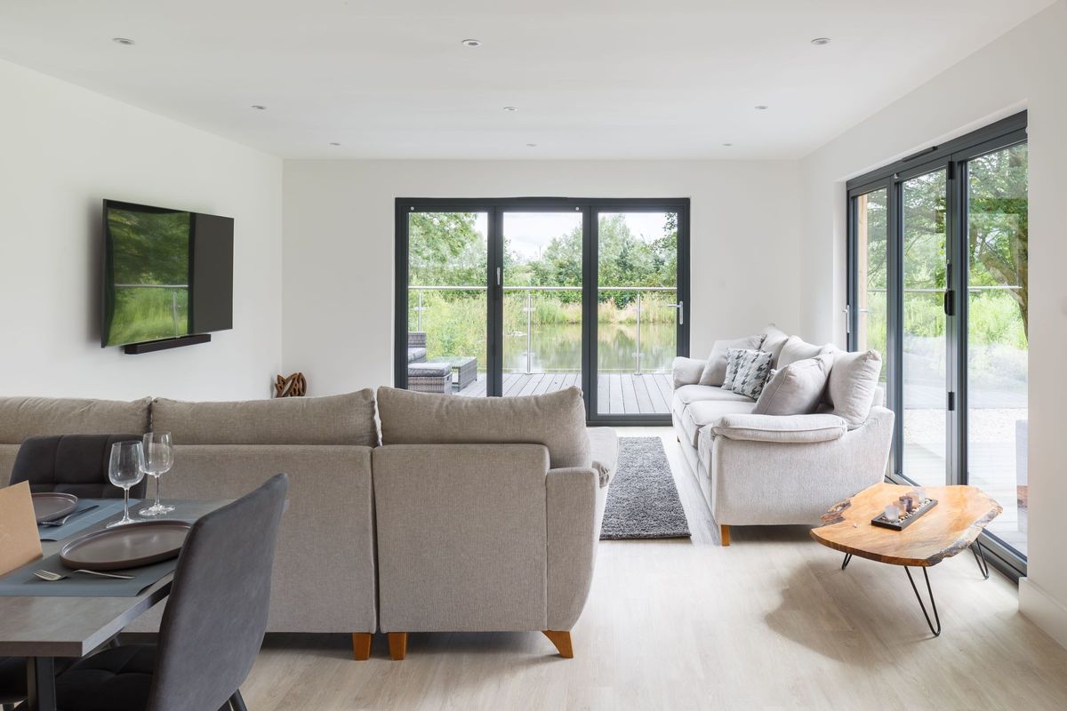 The living room leads onto a balcony overlooking the pond outside via bifold doors