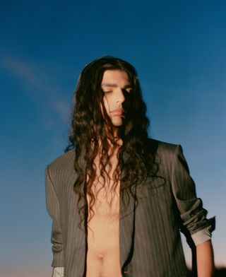 Man in suit jacket with no top photographed against evening sky