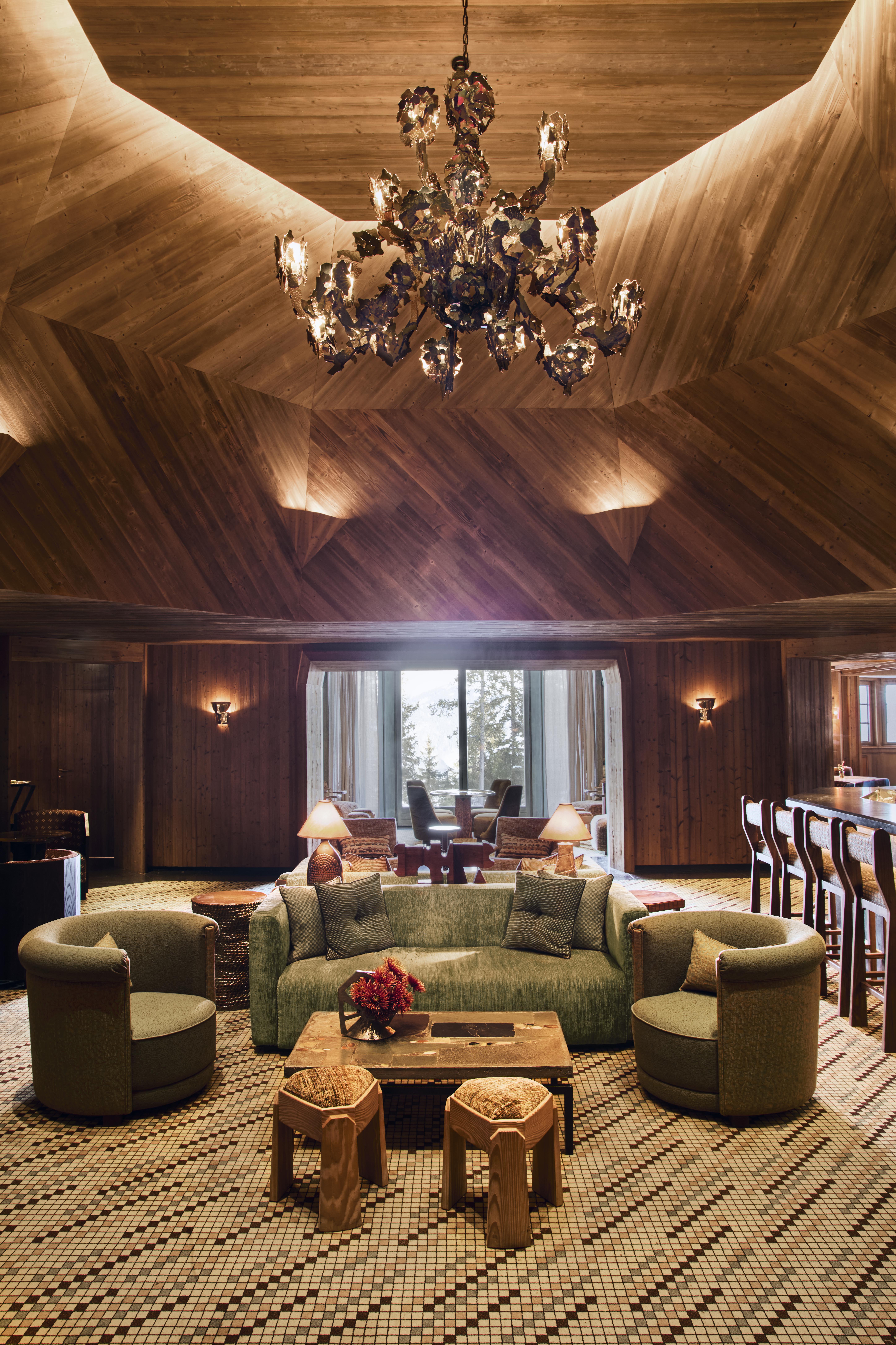 The elaborate, theatrical interiors of a ski chalet with wood wall paneling, plush textiles in different patternes, colors, and textures, plenty of paintings and sculptures adorning its halls, and a dimly lit atmosphere.