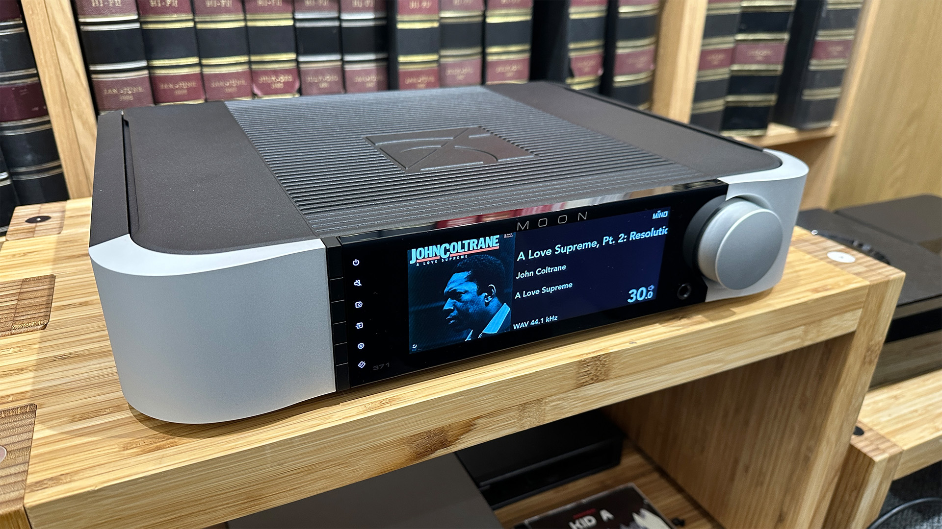 Moon 371 streaming amplifier on wooden hi-fi rack in front of bookcase, on display is John Coltrane