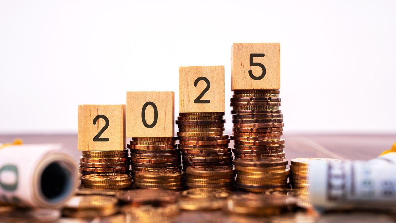 Four wooden blocks that spell out &#039;2025&#039; balanced on top of stacks of coins