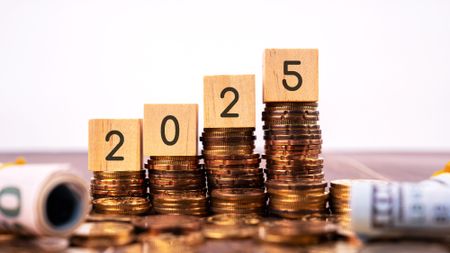 Four wooden blocks that spell out '2025' balanced on top of stacks of coins