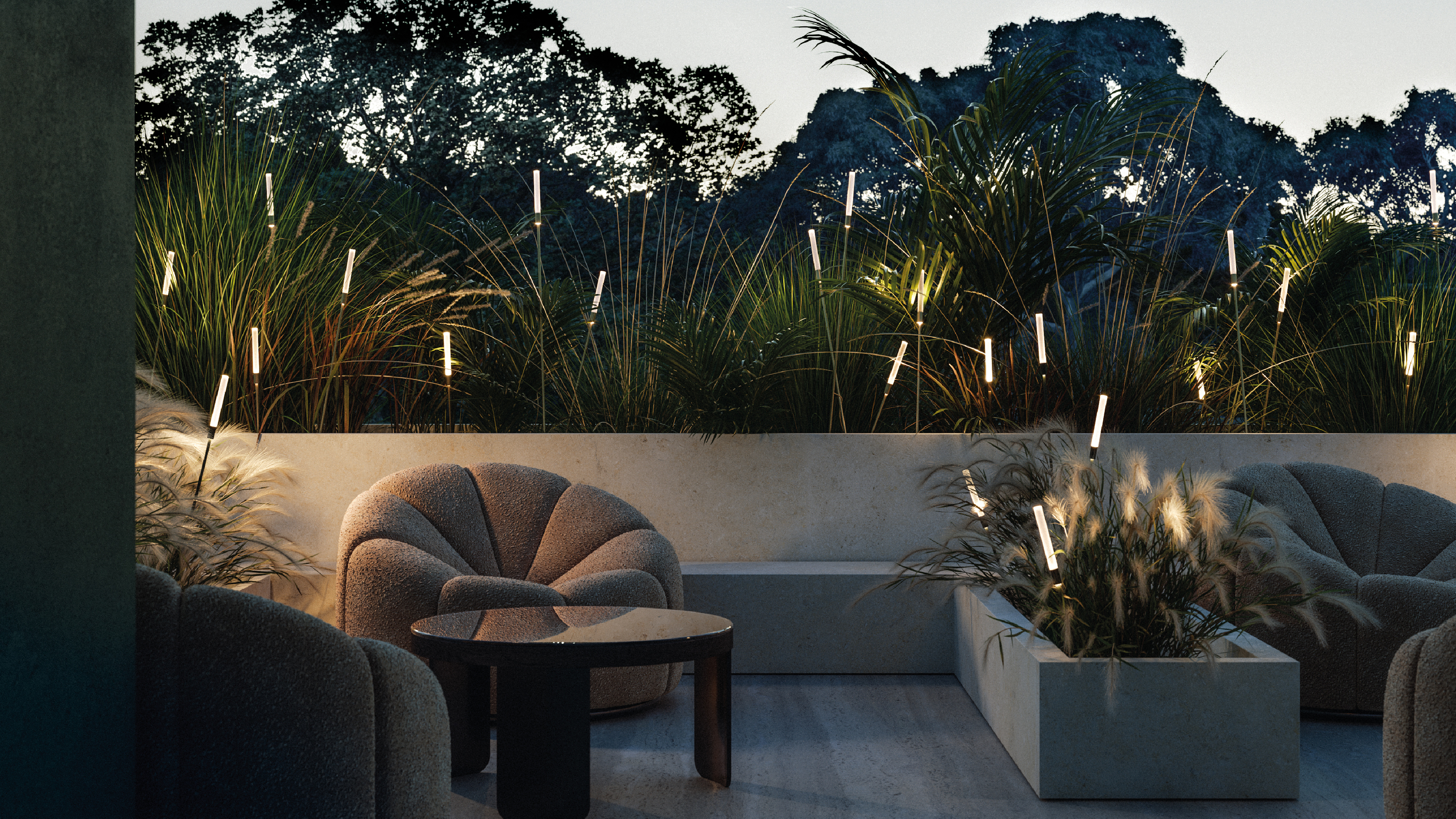 An outdoor patio at dusk with modern furniture, a concrete wall, and a border of grasses with &quot;firefly&quot; style lights on rods